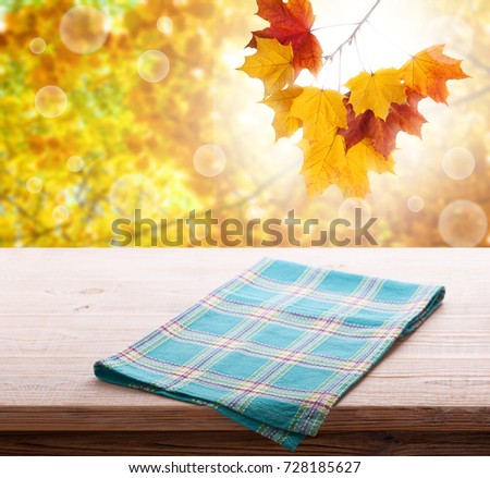Empty wooden deck table with tablecloth over bokeh autumn leaves background