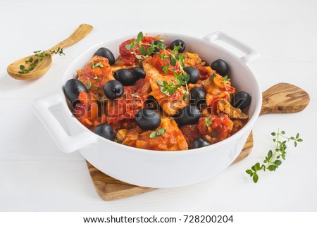 White fish stew with tomatoes, black olives and fresh thyme in a casserole on the wooden table.