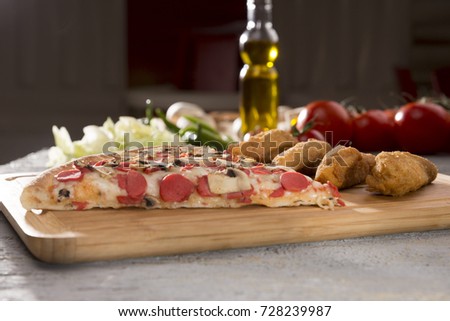 Delicious italian Pizza with sausage, Piece of Breaded, Fried crispy chicken breast nuggets, cherry tomato and lettuce on wooden bamboo plate. Rustic, damaged grey concrete textured background. 