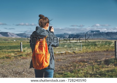 Girl in warm clothing photographing a beautiful landscape with background of mountains of Iceland.