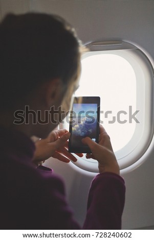 woman looking at sky with clouds and take a photo by phone from the airplane window.
