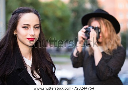 One blond girl photographer shooting brunette girl outdoors