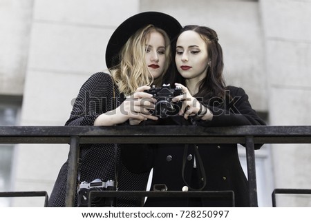 Half length portrait of couple of girls looking down at camera to see photo shoots. On the street,