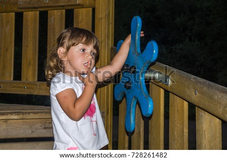 A small charming girl in a kerchief plays in a park on a playground