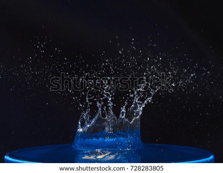 Splash of water crown on blue surface. Black background