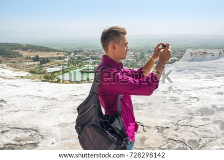 Young guy with backpack, tourist, takes pictures with his mobile phone view Pamukkale, Turkey