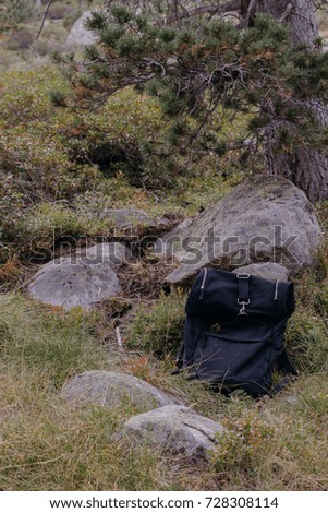 Big black backpack without logos laying in the forest near rocks. Travel and healthy lifestyle concept. Side view, selective focus and shallow DOF