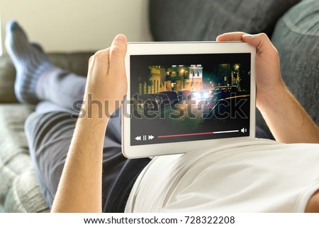 Online movie stream with mobile device. Man watching film on tablet with imaginary video player service. Royalty-Free Stock Photo #728322208