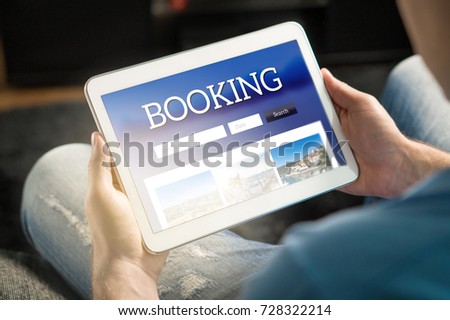 Booking app or website on tablet screen. Man searching hotel and flights for holiday and vacation with travel application. Person holding smart device in hand. 