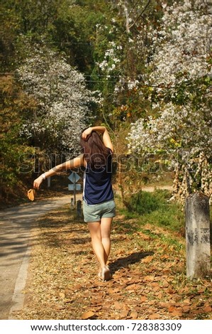 Model protrait on sleeveless shirt walking along street of white butterfly tree