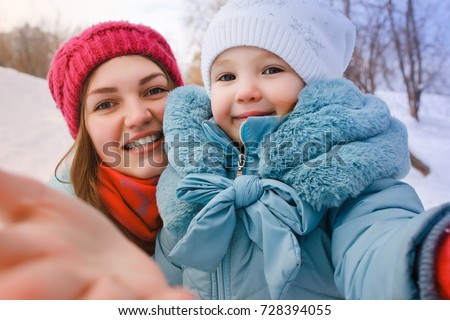 A young mother makes selfie and with her little daughter in the winter outside