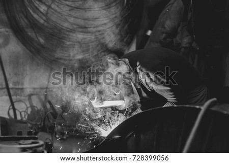 worker welding metal with sparks and smoke in the helmet
