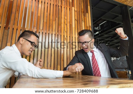 Asian businessman are arm wrestling on table at coffee shop. For Business and conflict or success concept.