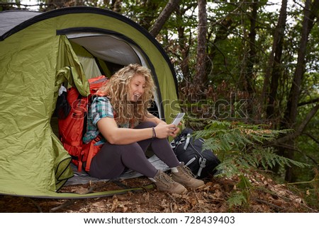 Camping woman in tent using smartphone looking at pictures photos