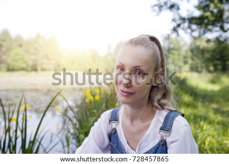 the beautiful slender young woman in a blue sundress and a white blouse on the bank of the forest lake in sunny day

