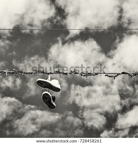 Sneakers hanging on the power line. Blue sky. Bad joke. Black and white photo.