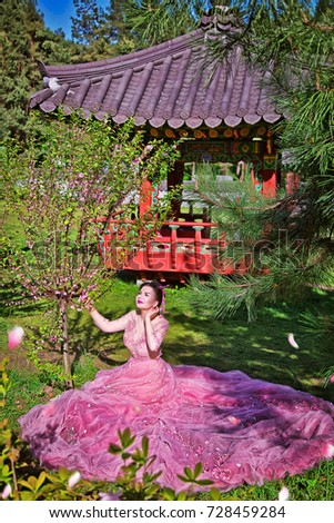 Woman in pink dress on background in Japanese temple in the park. Sakura (cherry) 