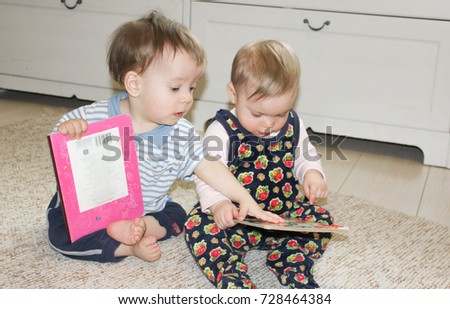 two small children sit on the floor and read books. Girl and boy look at the pictures in children's cardboard books.