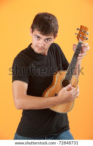 Serious Latino teen ukulele player on an orange background