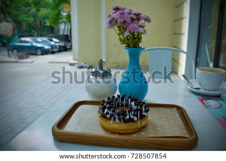 Hanukkah (Jewish festival) round donut (Hebrew word - sufganiyah) with chocolate topping on the wooden plate next to blue vase with autumn golden daisies and glass sugar bowl 