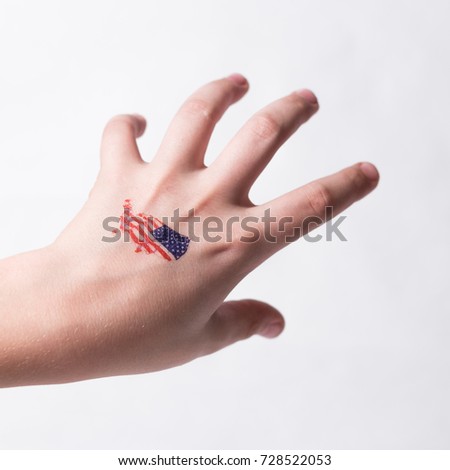 Square image: A hand of a teenager with a picture of the US flag is directed to take something on a white background.