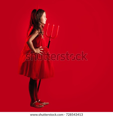 Side view full length picture of a girl in a devil halloween fancy dress on a red background