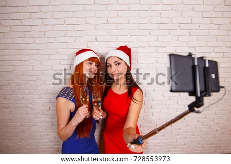 Young beautiful women in Santa caps having fun, drinking champagne, taking self portrait with a smartphone and selfie stick. Free space for text design.New Year, Christmas, party, technology concept