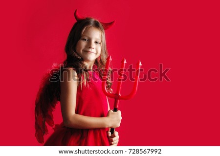 Side view picture of a happy girl in a devil halloween fancy dress on a red background