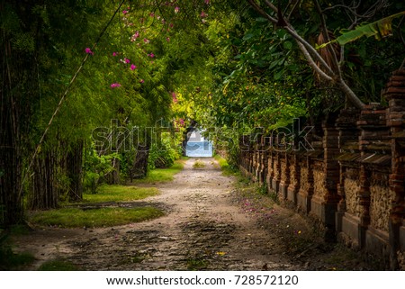 A real beautiful walkway trough nature. The romantic path is ending at the beach located in Bali. The tunnel with the balinese wall at the right side gives a fairytale effect. Royalty-Free Stock Photo #728572120