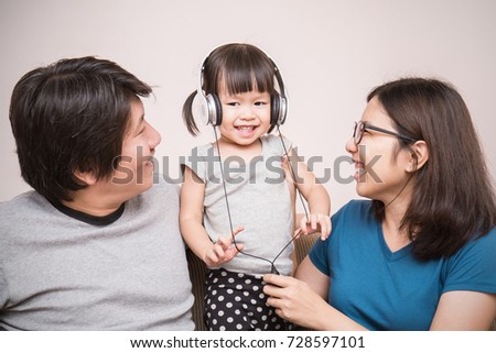 Closeup happy Asian parents and baby girl in sofa using tablet and headphones, Asian parents with toddler daughter girl listen to music in their living room.
