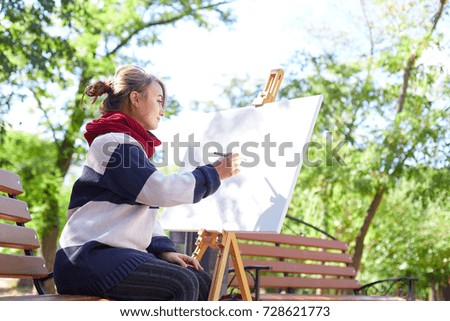 Beautiful artist draws a picture in a good mood outdoors.