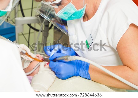 Close-up of a female dentist and her asleep lie teeth to a child using a drill and conduct treatment procedures against dental caries and plaque in a modern dental office
