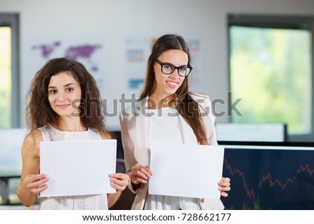 Two cheerful beautiful young business girls in the office with white sheets of paper