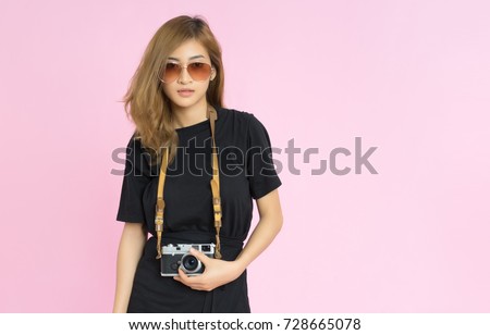 Fashion pretty young woman holds retro camera and wearing eyewear glasses, mini dress black over pink background