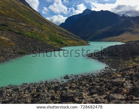 A green slope and rocks surround cool mountain water. Royalty-Free Stock Photo #728682478
