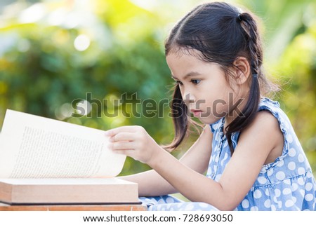 Cute asian little child girl reading a book in outside in nature background