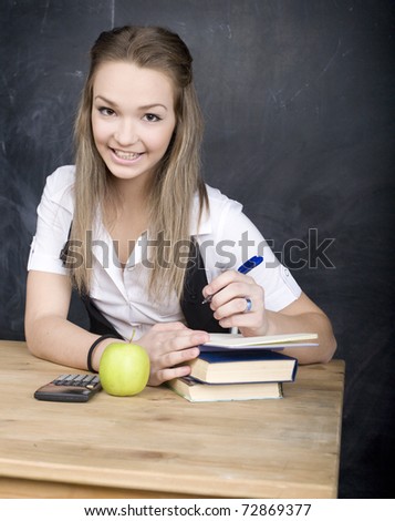portrait of happy cute student with calculator, book, pen and green apple near blackboard