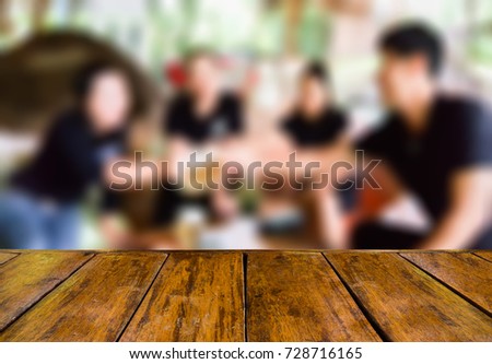 empty wooden table and blurred image of people clink their beer glasses in the restaurant