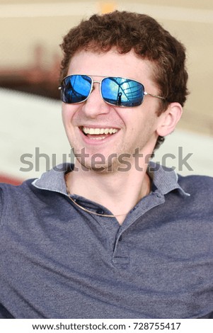 Young smiling man in sunglasses on the beach. The reflection in the glasses the bright blue sky.