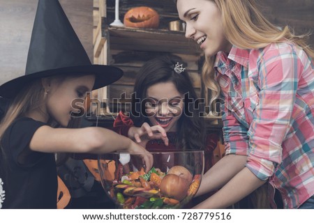 Children in costumes of monsters on Halloween to reach for sweets, which lie in the vase that their mother brought to them
