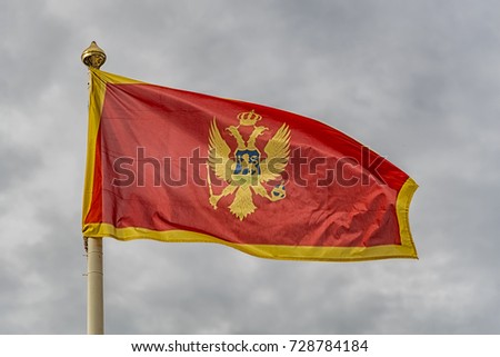 The flag of Montenegro fluttering in the wind against a cloudy sky background.