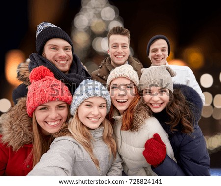 friendship, holidays and people concept - group of happy friends taking selfie outdoors over christmas lights background
