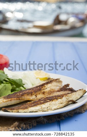 Smoked Delicious Grilled Fillet Fish mackerel (uskumru) serving with plate, tomato, sliced onion, green arugula salad and lemon on wood table background. Principally belonging to family Scombridae.