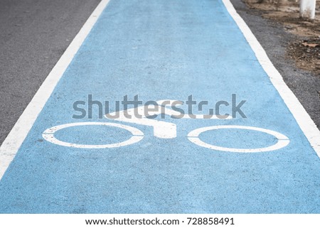 Close up on white bicycle sign or icon on blue bike lane with white fence on side of road to protect people walking in park.