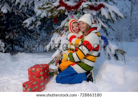 Young mother plays with child near the Crismas tree in the similar jackets