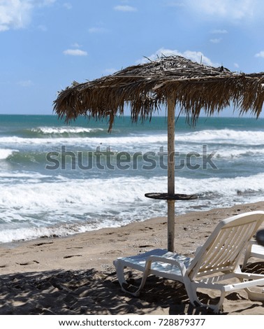 A sun bed and an umbrella on a beautiful deserted beach close to sea waves