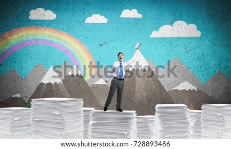Businessman keeping hand with book up while standing on pile of paper documents with drawn landscape on background. Mixed media.