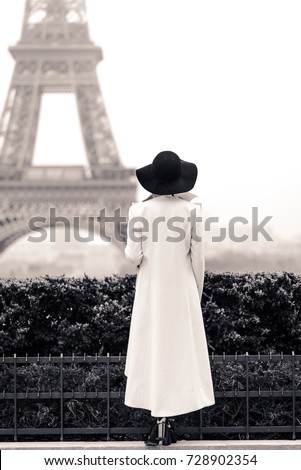Woman in white coat and black hat in Paris in front of the Eiffel tower. Black and white picture