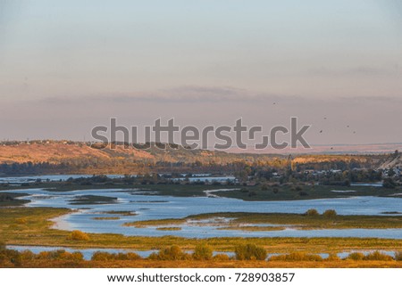 Autumn landscape. View from the top of the mountain. Natural forms in transitional period: gloomy mountains, cold river, yellowed grass, dark sky.