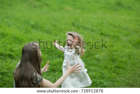 Portrait of a beautiful cheerful little girl with blond hair running with a smile in the arms of her mom on the park background. Happy family walking and playing in the park.